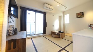 A room with tatami flooring, a sliding door, a flat-screen TV, an air conditioner, a small wooden table, and a cushion. - The Sorapia Tokyo (Tokyo)