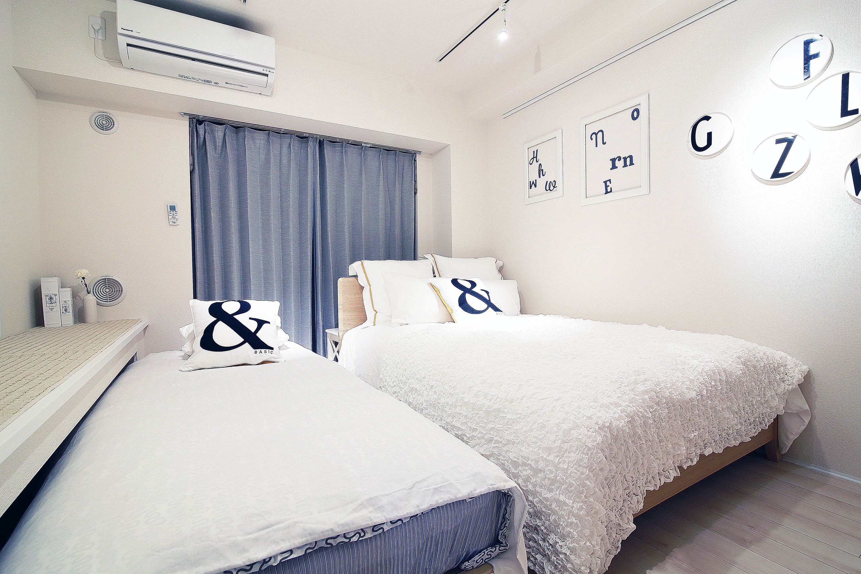 Quarto com duas camas, ventilador de teto, ar condicionado e janela com cortinas.