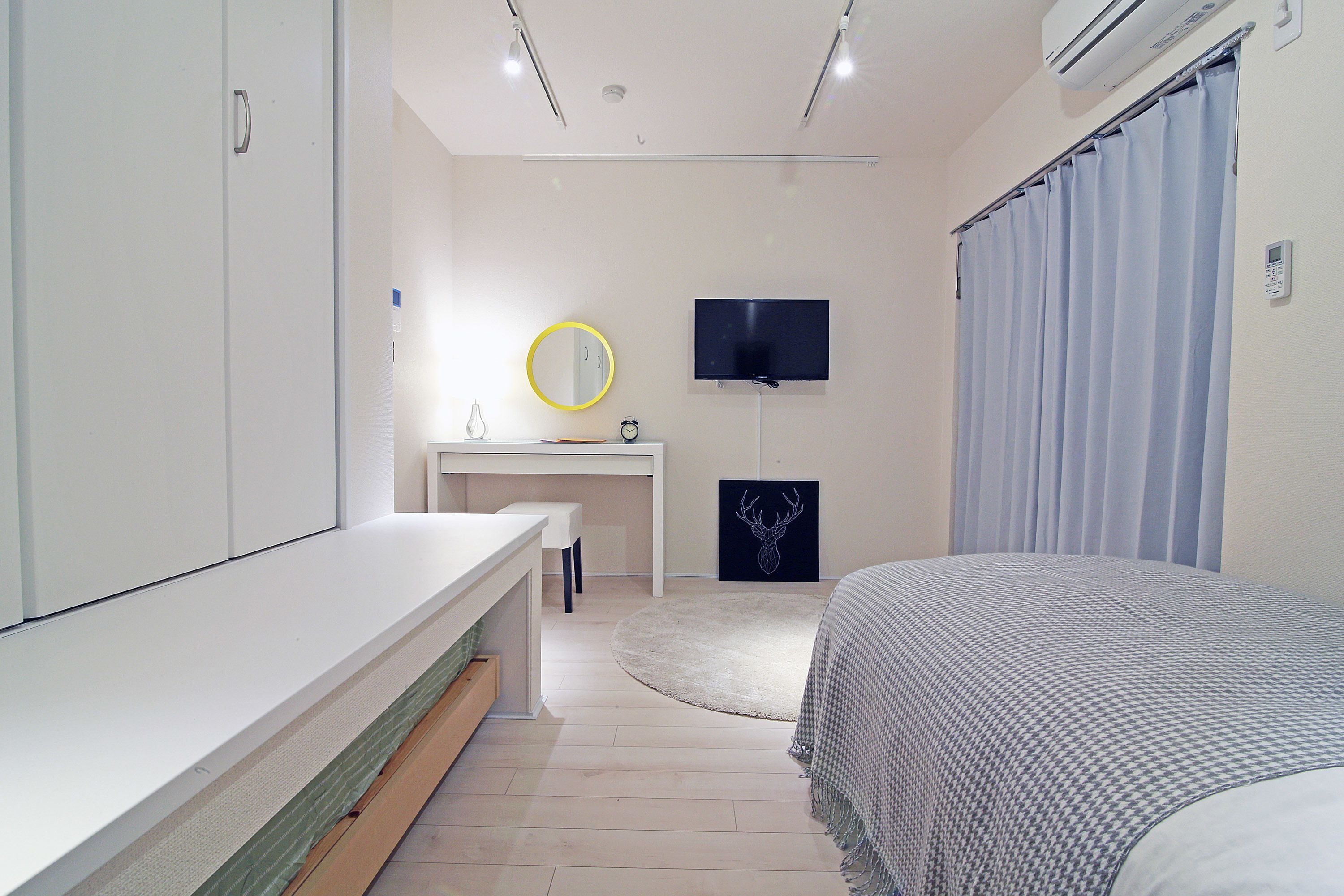 Une chambre à coucher comprenant un lit, un bureau, une chaise, un miroir, une télévision et une fenêtre avec des rideaux.