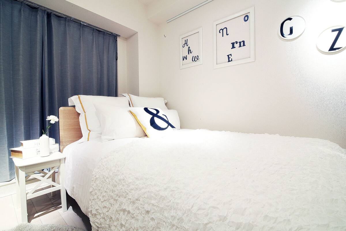 A neatly arranged bedroom with a large bed, a bedside table with a lamp, and a wall with decorative letters.