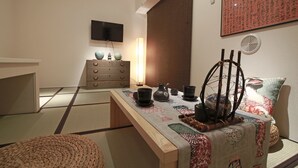 A traditional Japanese room with tatami flooring, a low wooden table with tea ceremony utensils, a television on the wall, and a sliding door. - The Sorapia Tokyo (Tokyo)