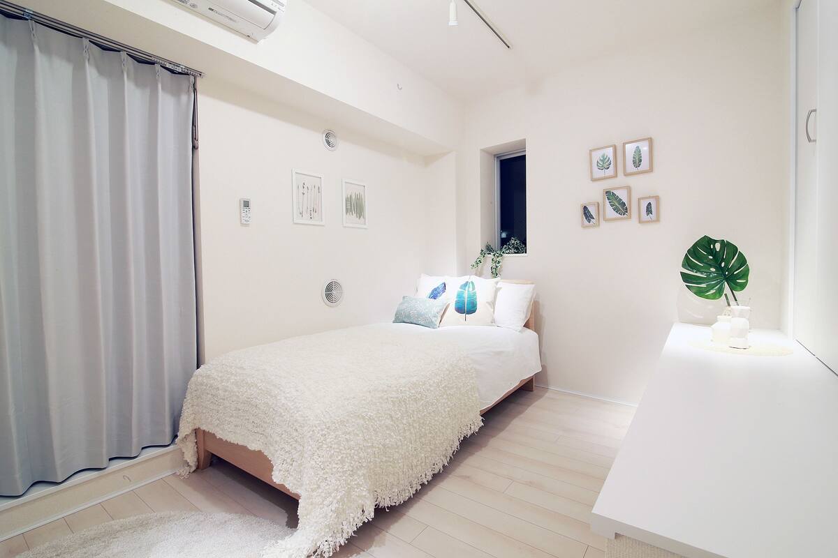 A minimalist bedroom with a bed, a bedside table, a window, and wall art.