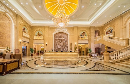 A grand lobby with a central reception desk, a large chandelier, and a grand staircase.