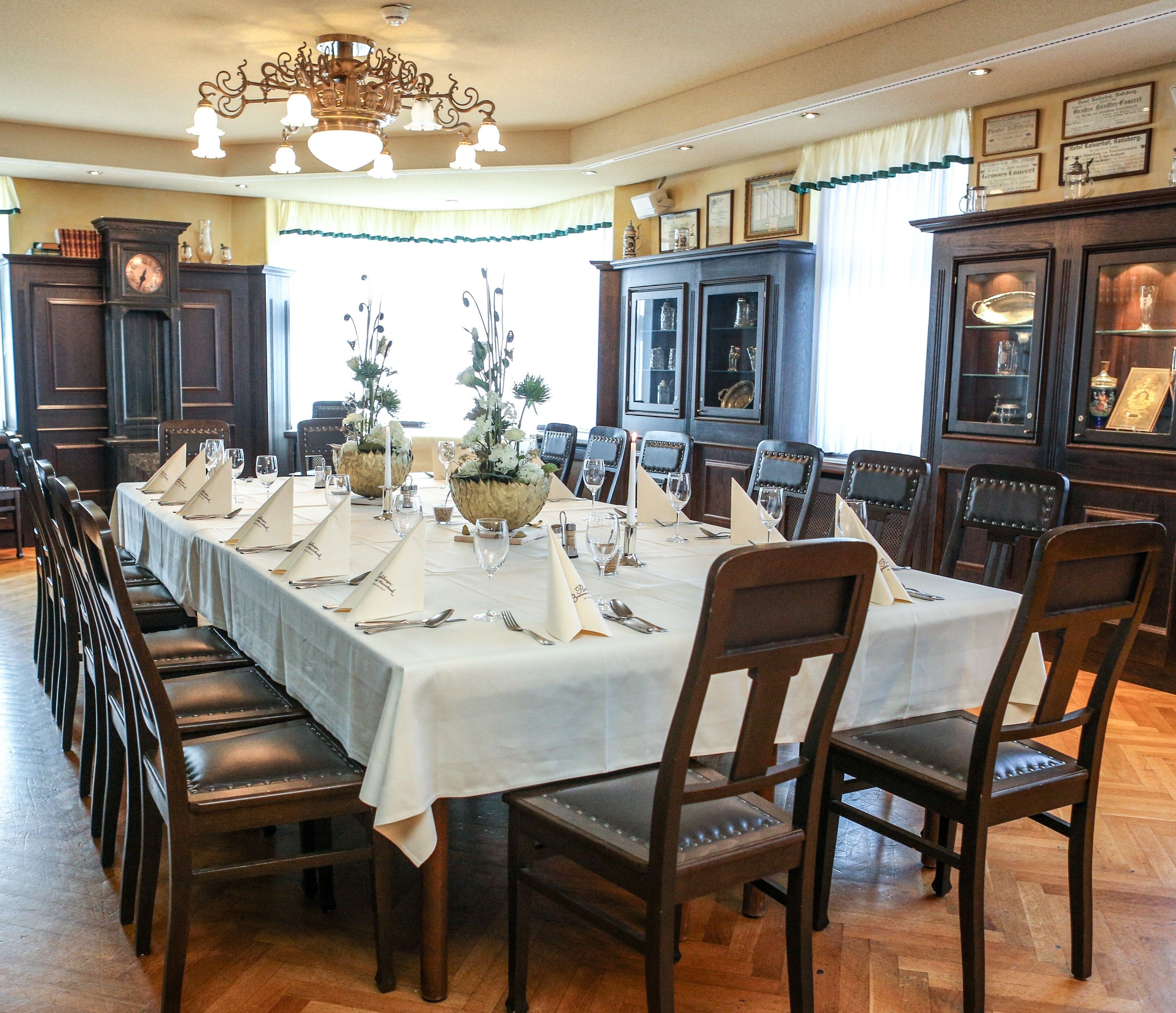 Uma sala de jantar formal com uma longa mesa posta para refeição, cadeiras de madeira e um lustre.