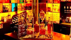Un bar con estantes llenos de botellas de licor, un hogar central y un tablero de menú.