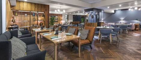 Un comedor espacioso con varias mesas y sillas, piso de madera e iluminación moderna en el techo.