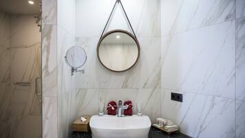 Une salle de bain avec un mur en marbre, un miroir rond, un lavabo avec deux serviettes rouges et un verre posé sur le comptoir.