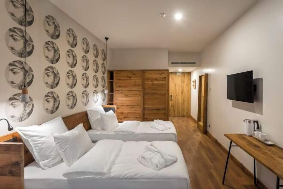Ein Hotelzimmer mit zwei Betten, einem Holzschrank, einem Fernseher und einer Wand mit kreisförmigem Muster.