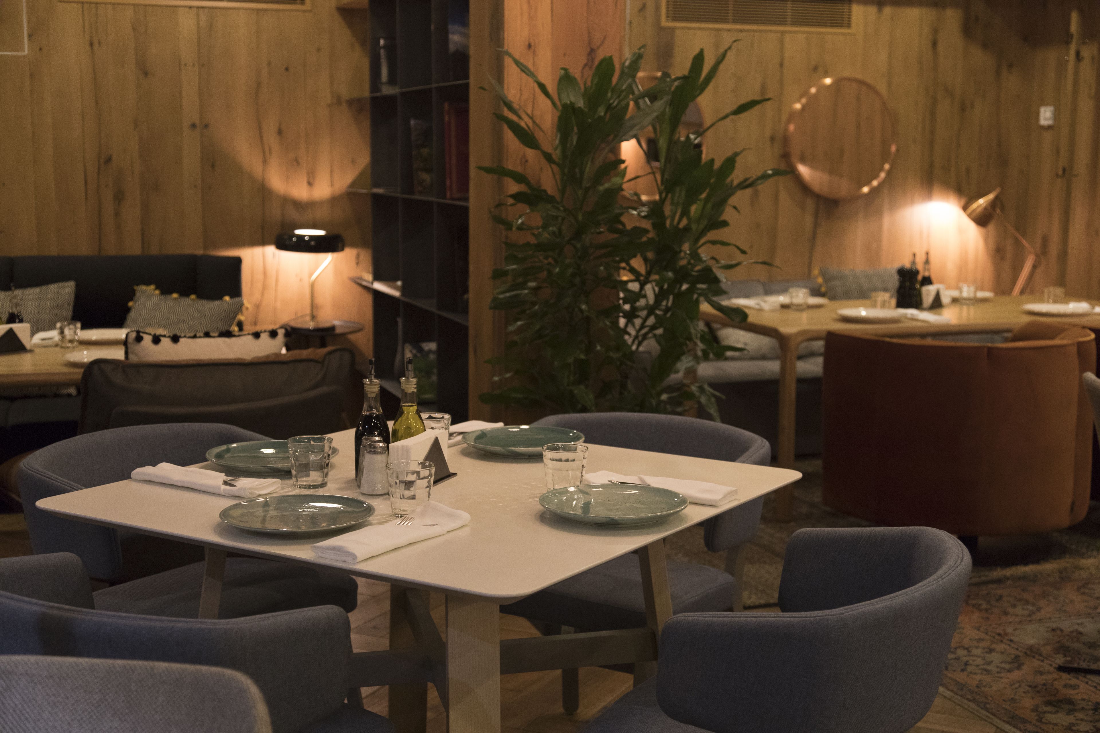 A dining area with a wooden wall, a table set for four, and a potted plant.