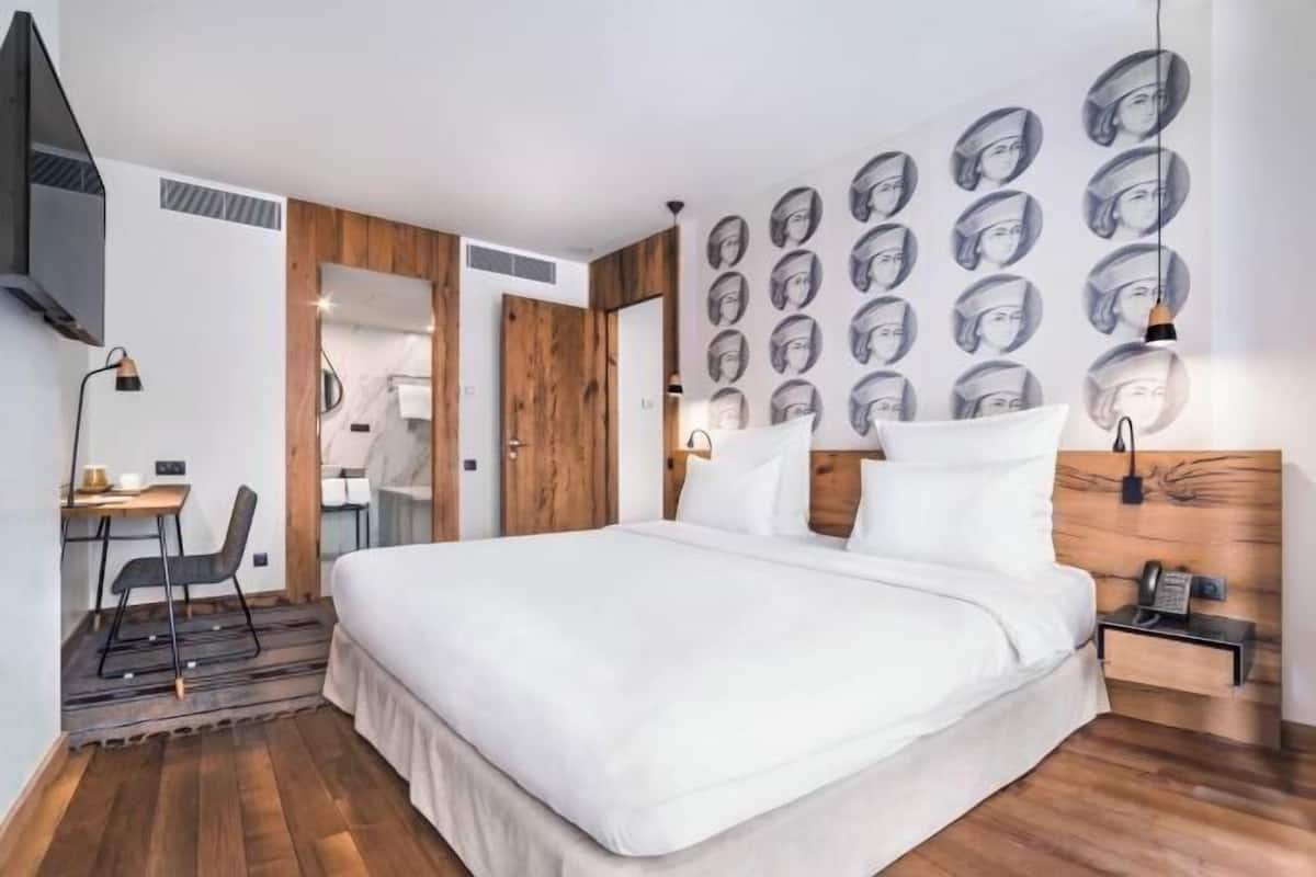 Ein modernes Hotelzimmer mit einem großen Bett, einem Schreibtisch und einer Wand mit mehreren Porträtfotos.