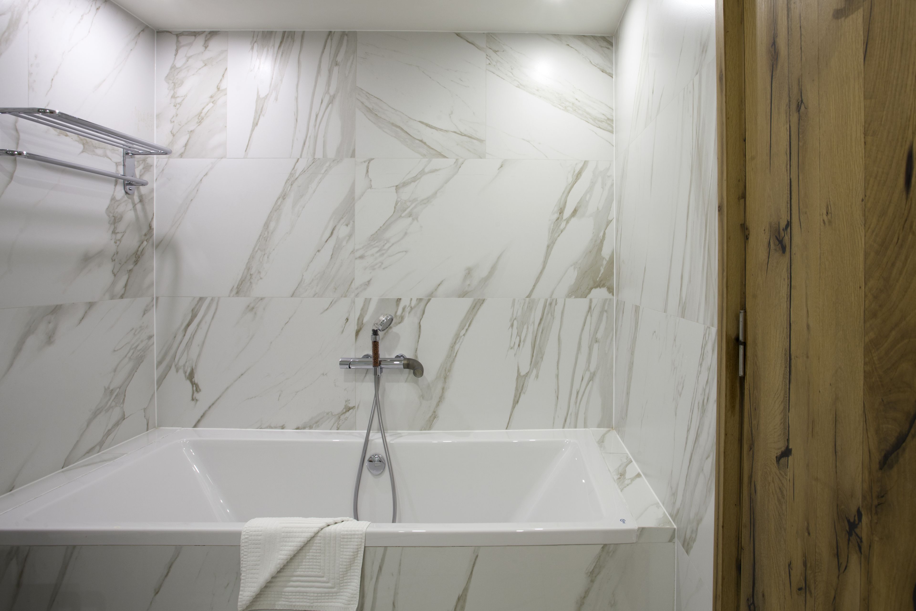 Un baño moderno con pared de mármol, puerta de madera y bañera blanca.