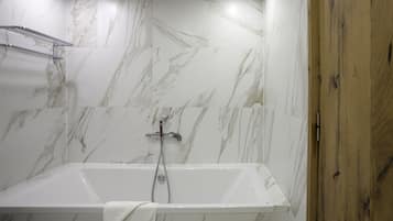 Un baño moderno con pared de mármol, puerta de madera y bañera blanca.