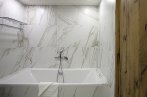 Un baño moderno con pared de mármol, puerta de madera y bañera blanca.