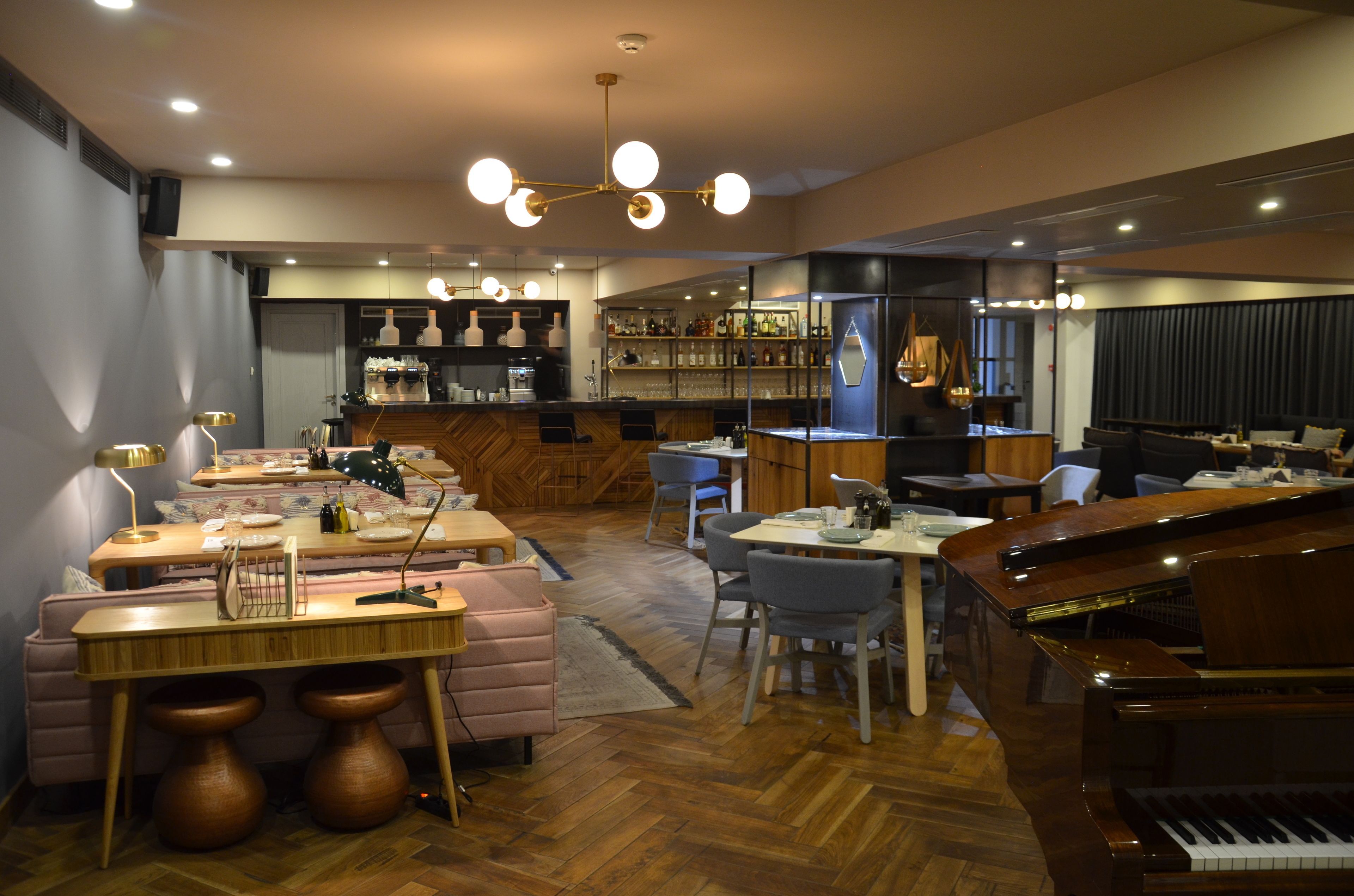 Un vaste espace de vie comprenant un piano, un bar et un coin repas avec des meubles en bois et une grande fenêtre.