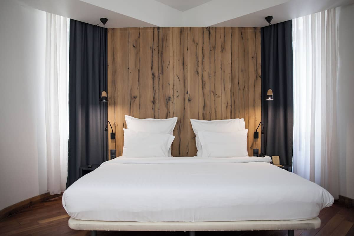 Ein modernes Hotelzimmer mit einem großen Bett, einer Wandpaneele aus Holz und zwei Nachttischlampen.