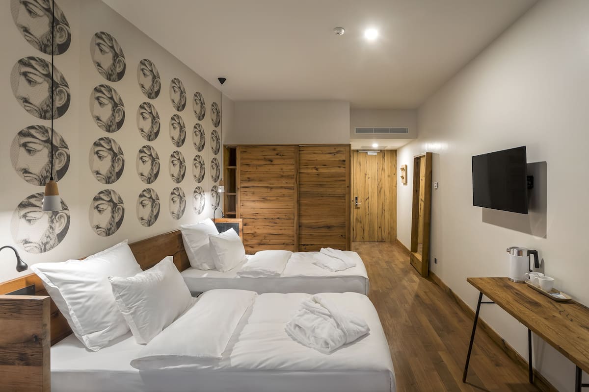 Ein modernes Hotelzimmer mit zwei Betten, einem Holzschrank, einem Fernseher und einem Holztisch mit einer Kaffeemaschine.