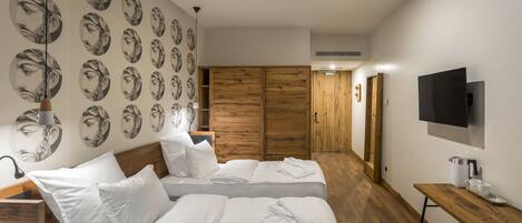 Una habitación de hotel moderna con dos camas, un armario de madera, un televisor y una mesa de madera con cafetera.