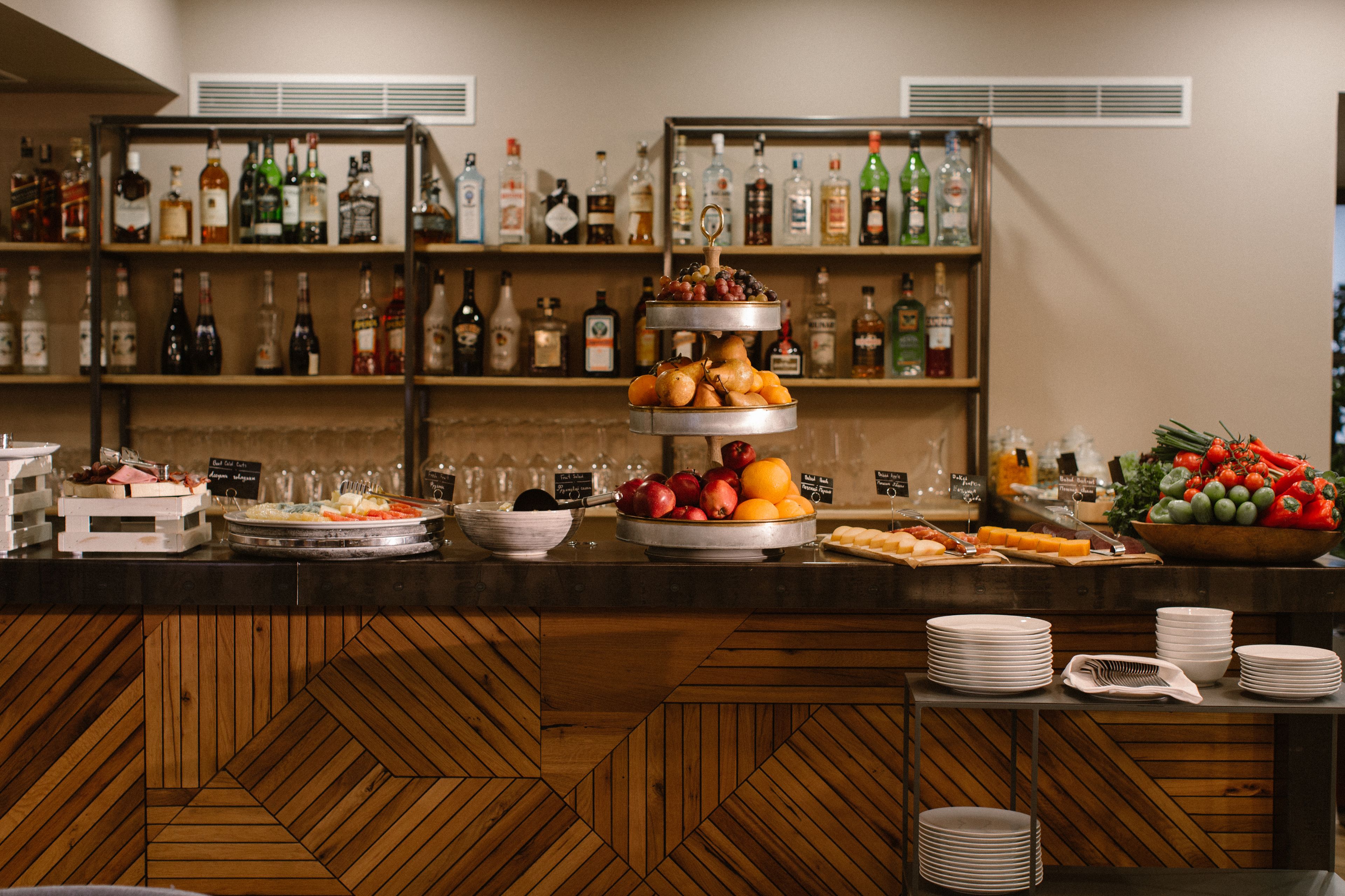 A buffet area with multiple food stations, including a fruit display and a variety of beverages on shelves.