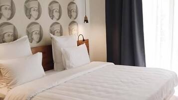 Habitación de hotel con una cama grande, cabecero, mesita de noche y pared con un diseño repetido de fotografías.