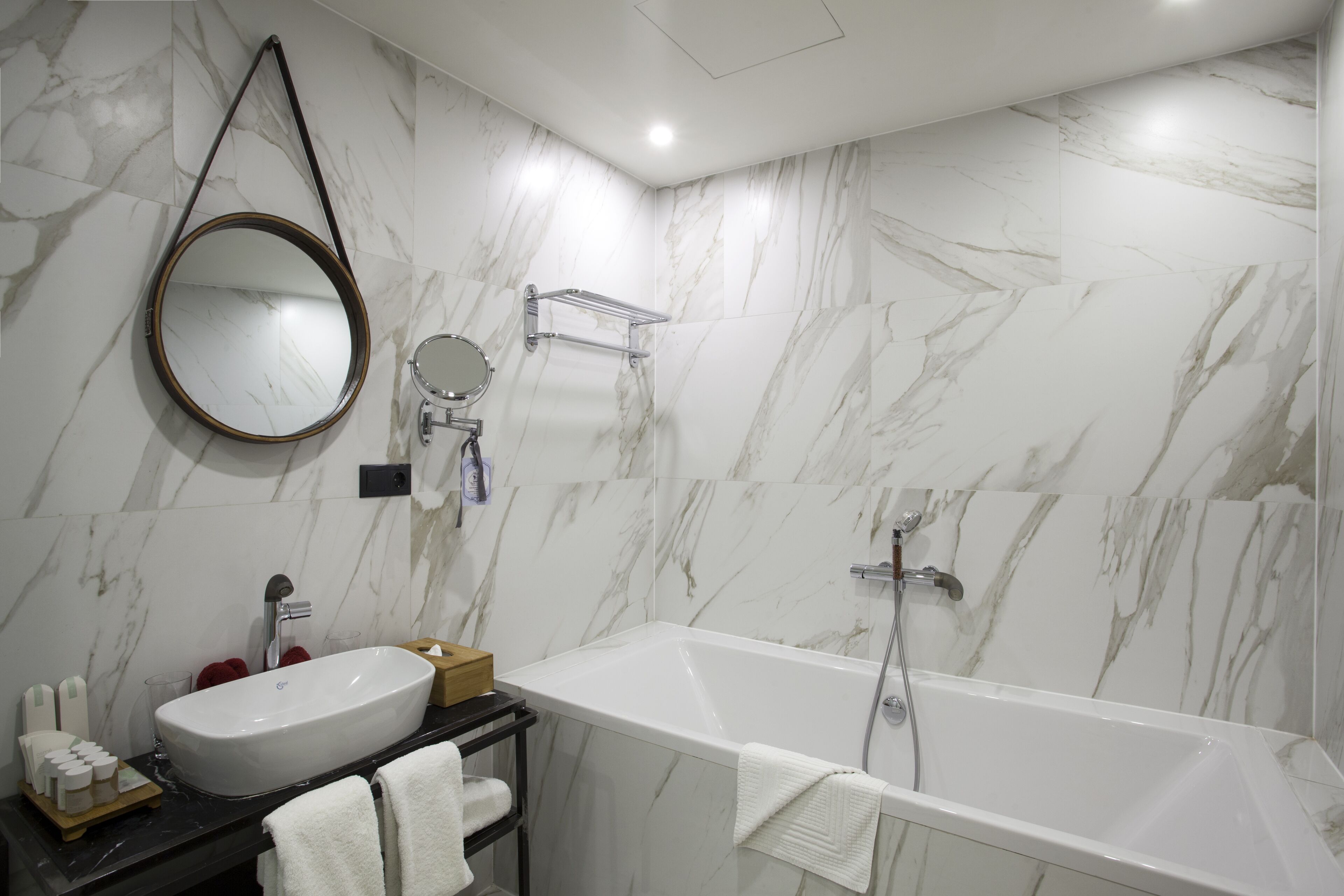 A modern bathroom with a white marble sink, a large mirror, a bathtub, and a towel rack.