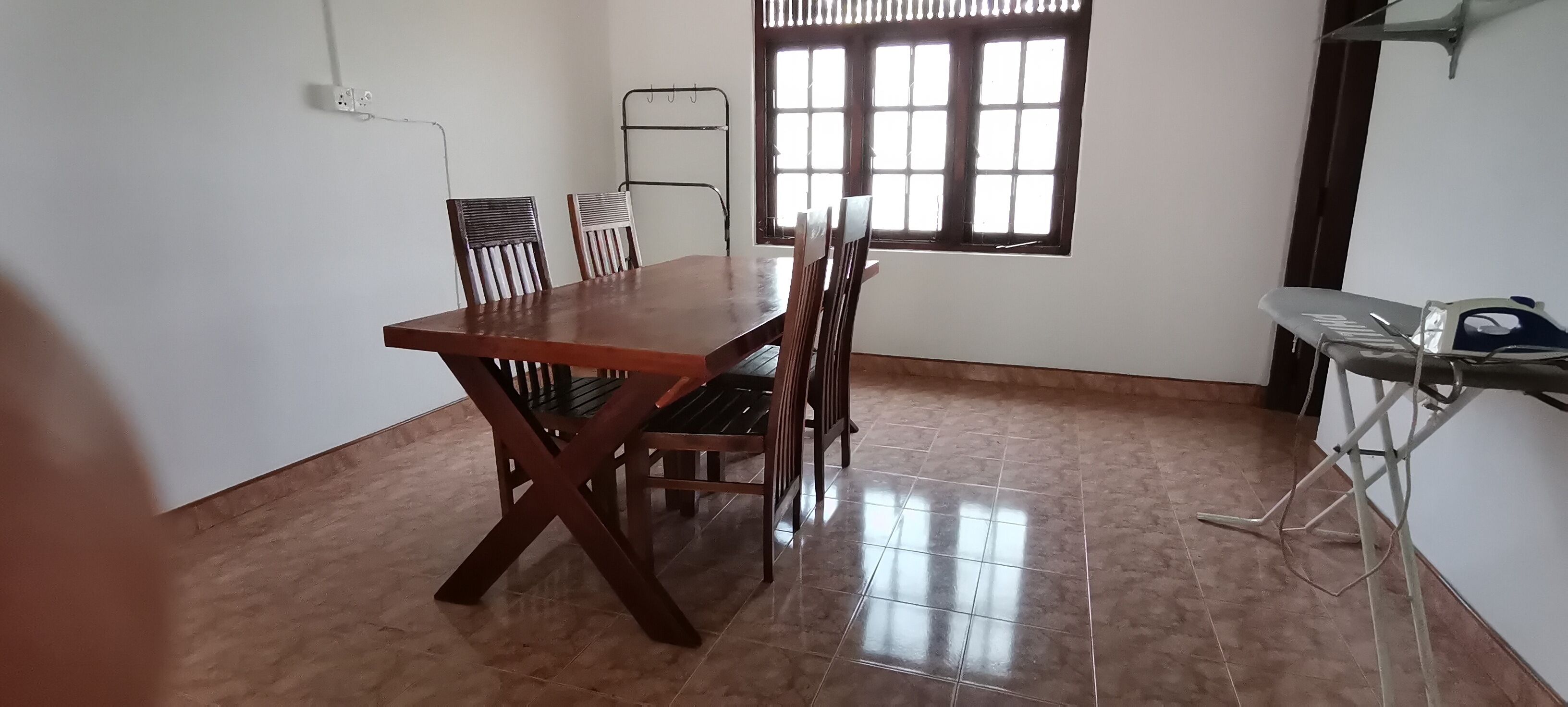 A dining area with a wooden table and chairs, a window with blinds, and a clothes drying rack.