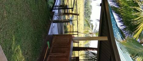 A covered outdoor seating area with a wooden structure and a roof, surrounded by grass and palm trees.