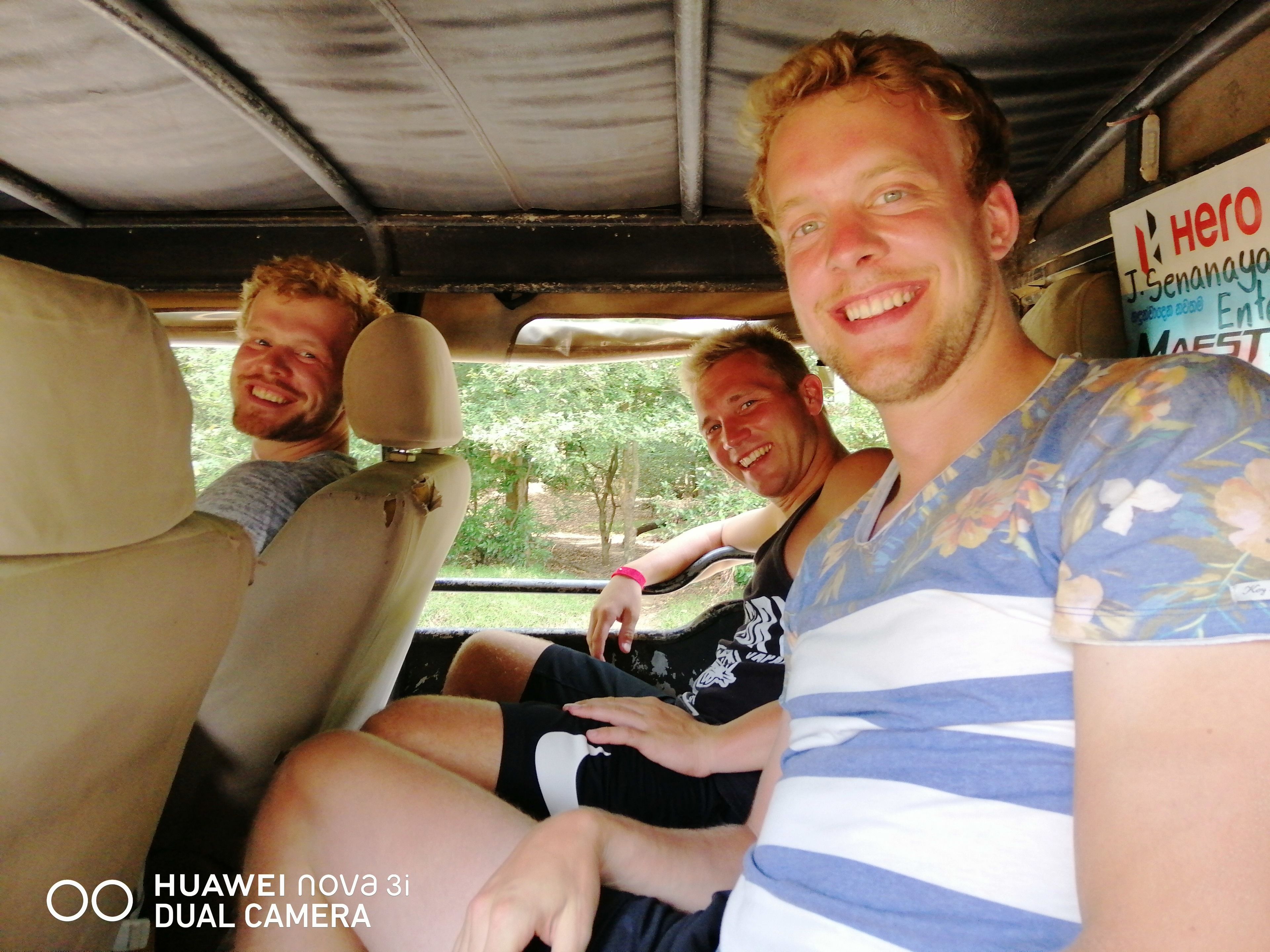 Three people seated in a vehicle with a sign reading "Hero" in the background.