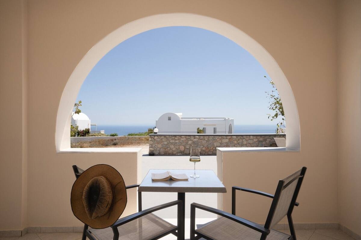 Un balcón con mesa, sillas y vistas al mar y edificios blancos.
