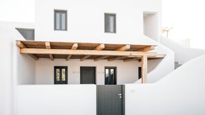 A modern building with a wooden pergola, a dark entrance door, and a staircase leading to an upper level. - Villa Libertad (Santorini)