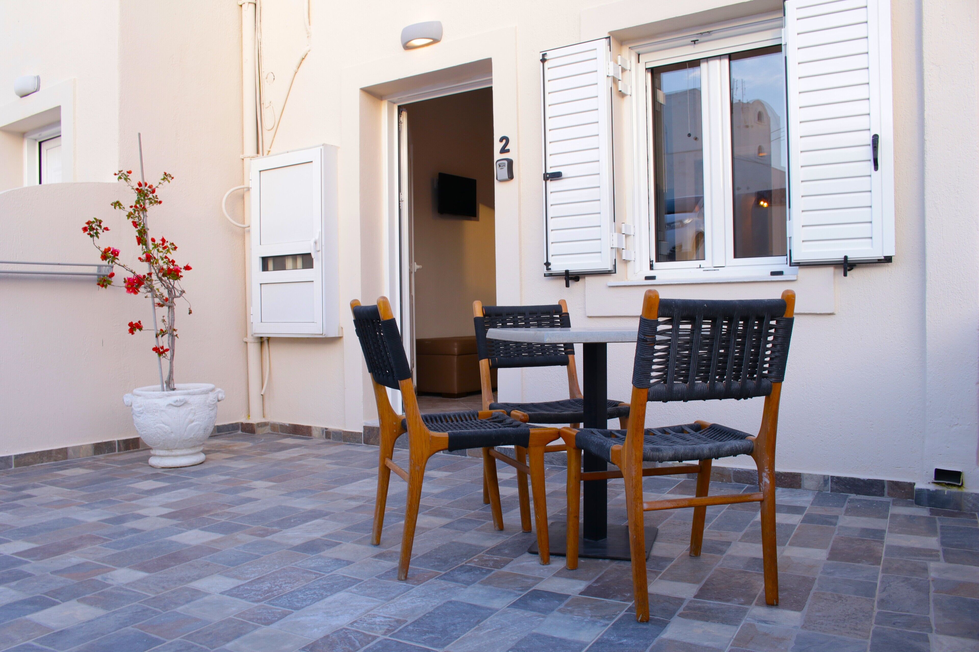 An outdoor seating area with a table and chairs, a potted plant, and a door leading to an interior space.