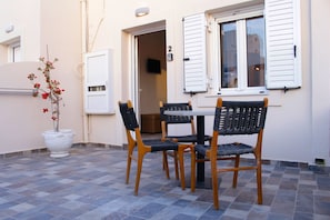 An outdoor seating area with a table and chairs, a potted plant, and a door leading to an interior space. - Villa Libertad (Santorini)