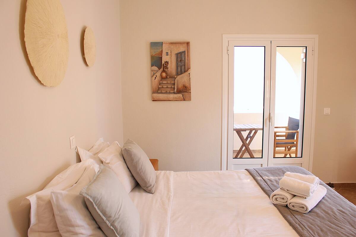 Un dormitorio con cama, almohadas, un cuadro y vistas a un espacio exterior con mesa y sillas.
