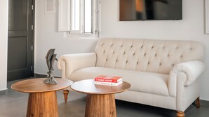 A living room with a beige sofa, two wooden tables, and a decorative sculpture. - Villa Libertad (Santorini)