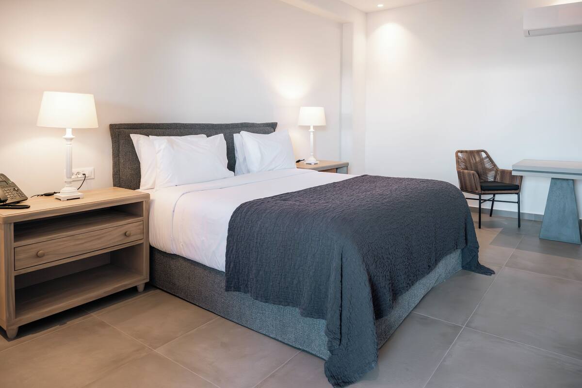 Una habitación de hotel ordenada con cama, mesitas de noche, una silla y un escritorio.