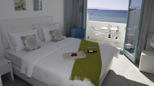 A modern hotel room with a bed, a green throw, and a view of the sea through a glass door. - Amaryllis Beach Hotel (Paros)