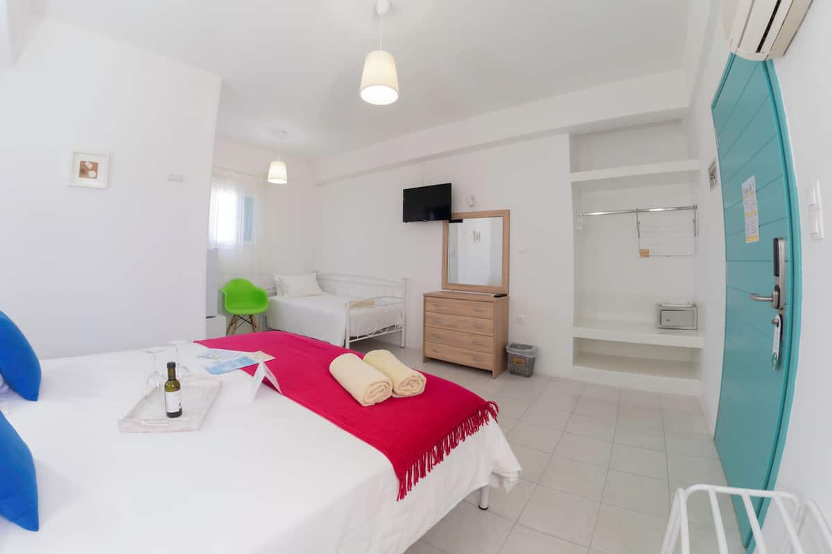 A hotel room with a bed, a dresser, a mirror, a chair, a TV, and a bathroom with a shower and toilet.