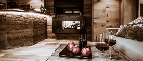 A cozy room with a wooden interior, a fireplace, a sofa, and a table with a bottle of wine and glasses.