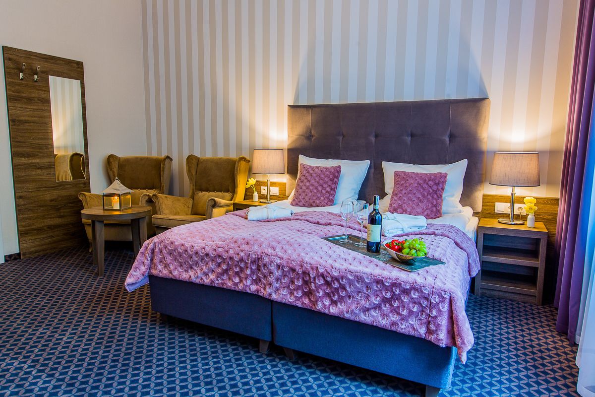 Una habitación de hotel con una cama grande, dos mesitas de noche, una silla, un espejo y una pared a rayas.