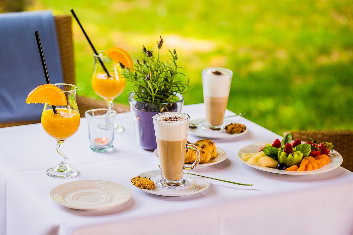 Una mesa al aire libre con diferentes bebidas, un plato de fruta y una planta pequeña.