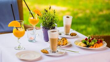 Una mesa al aire libre con diferentes bebidas, un plato de fruta y una planta pequeña.