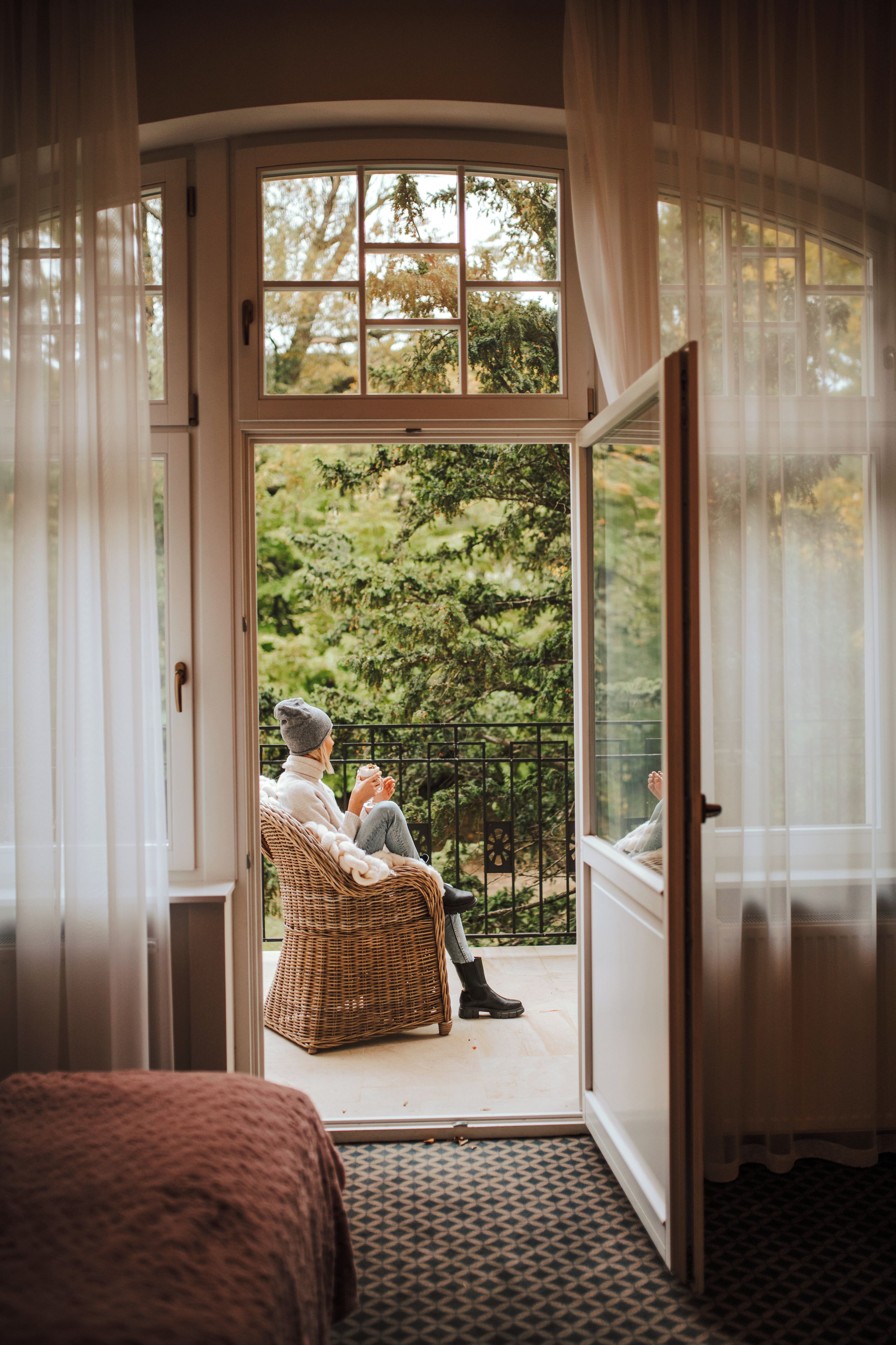 A room with a large window, a wicker chair, and a bed.