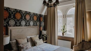 A bedroom with a bed, a nightstand, a lamp, a window with curtains, and a plant.