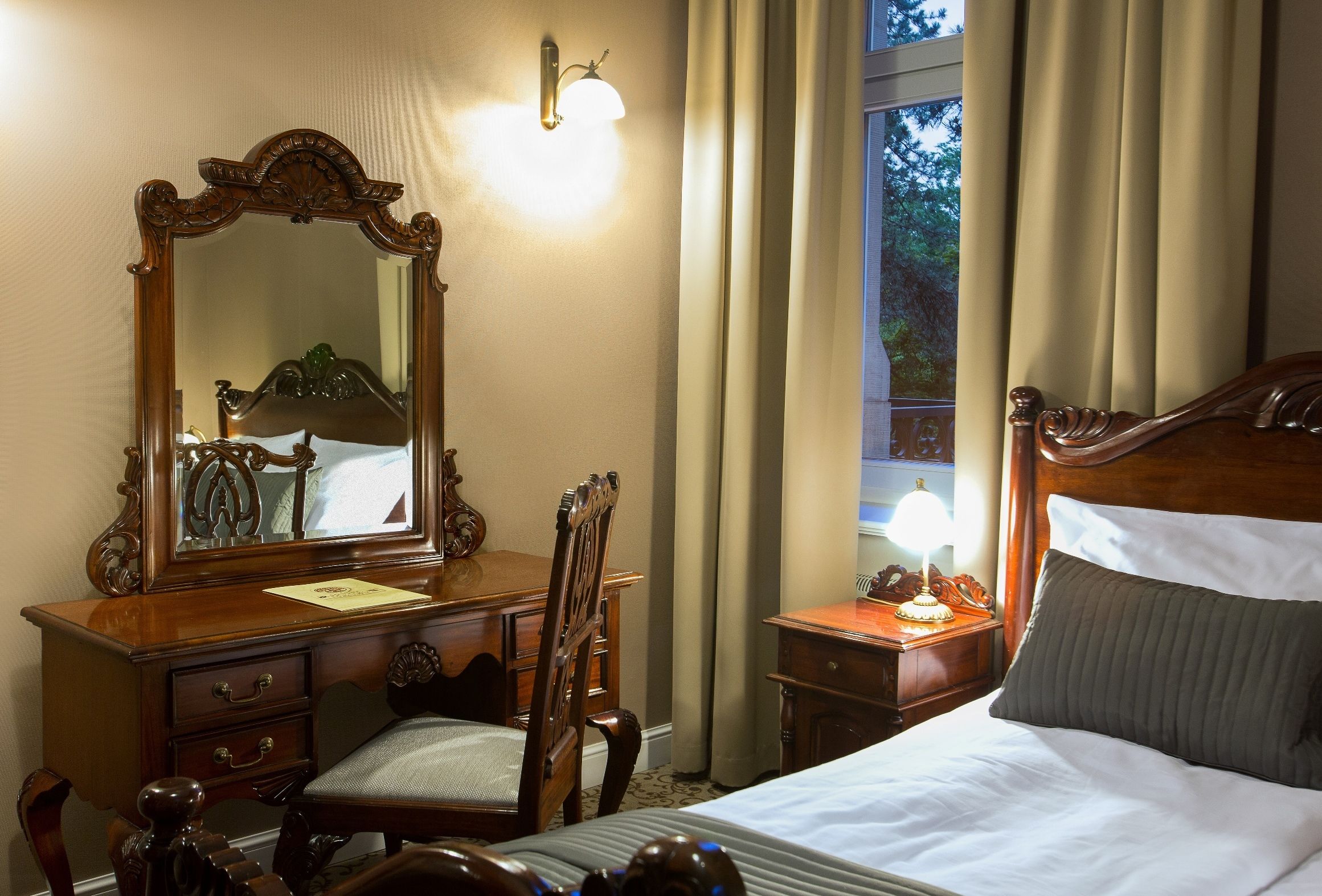 A hotel room with a large wooden bed, a wooden dresser with a mirror, a chair, and a nightstand with a lamp.