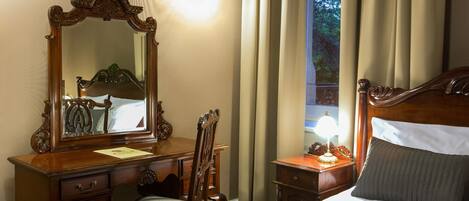 Una habitación de hotel con una cama grande de madera, un aparador de madera con espejo, una silla y una mesita de noche con lámpara.