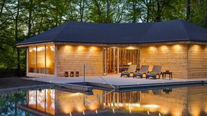 A modern wooden cabin with a pool, featuring a deck with lounge chairs and a dining area.