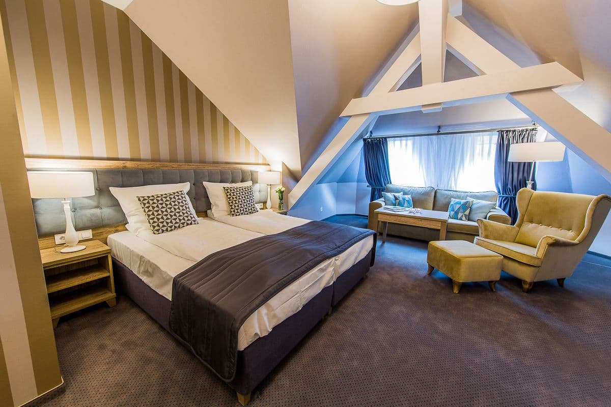 A modern hotel room with a large bed, a sofa, a chair, and a desk.