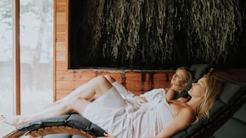 Twee personen liggen op een ligstoel in een kamer met een houten wand en een raam.