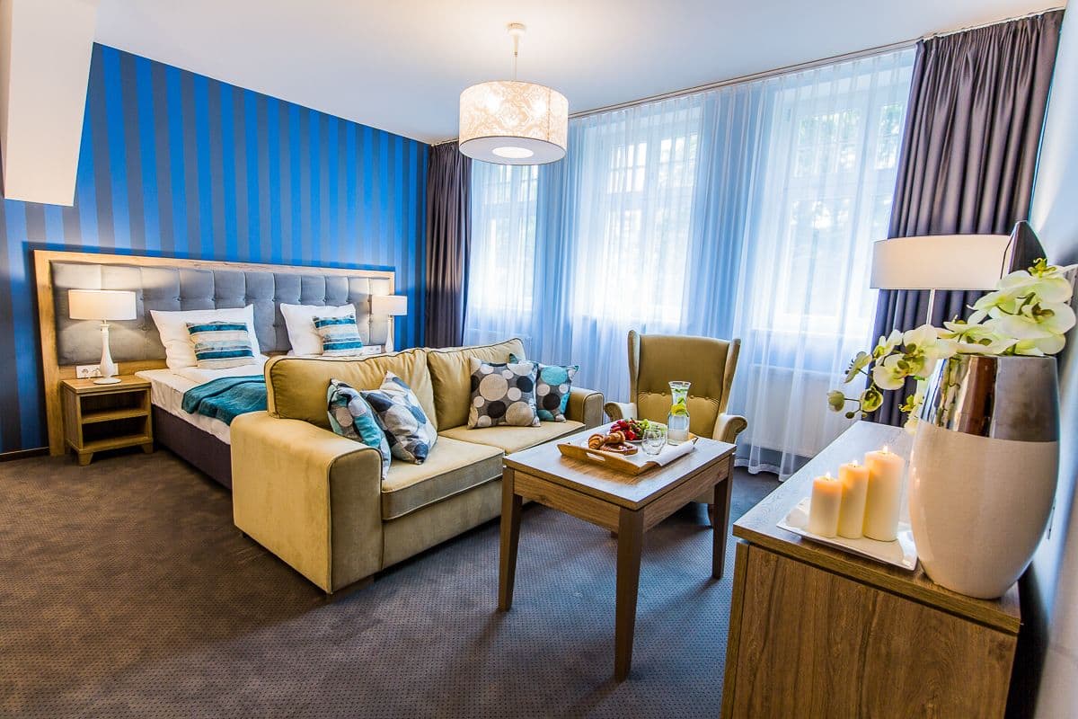 A hotel room with a bed, a sofa, a coffee table, and a lamp.