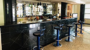 A bar area with a black marble countertop, multiple stools, and a variety of liquor bottles. - Golden Park Hotel (Luanda)