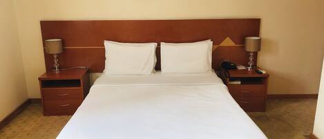 Una cama bien hecha con sábanas blancas, dos mesitas de noche con lámparas y un cuadro en la pared.